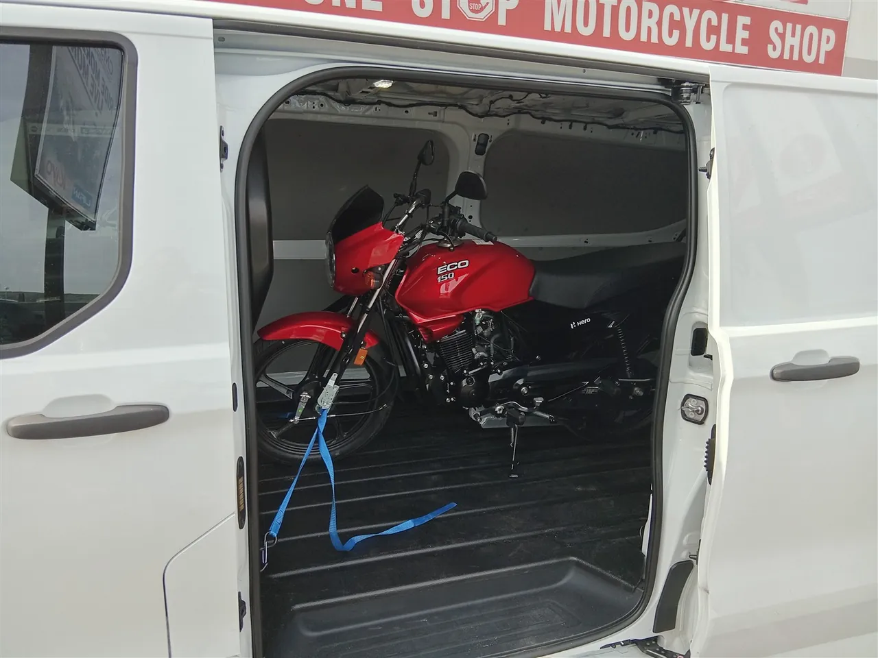 Red Hero Eco 150 inside the van near a motorcycle shop